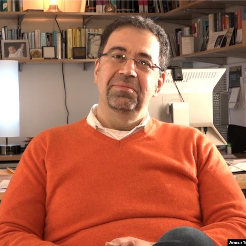 Image of a man in an orange jumper wearing glasses smiling at the camera
