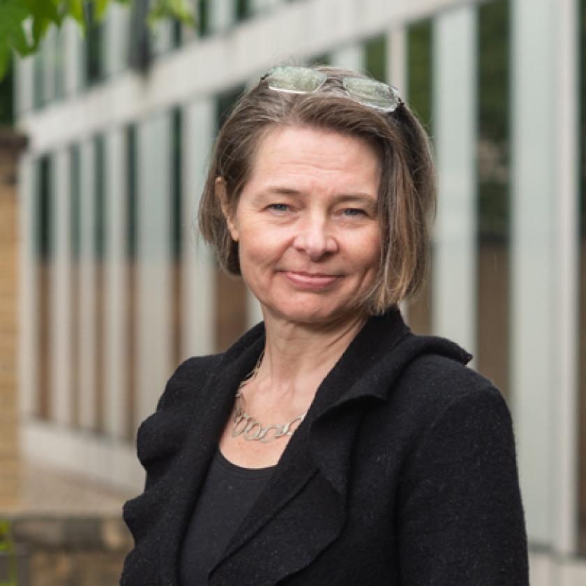 Image of a woman in front of a building and some greenery smiling  at the camera
