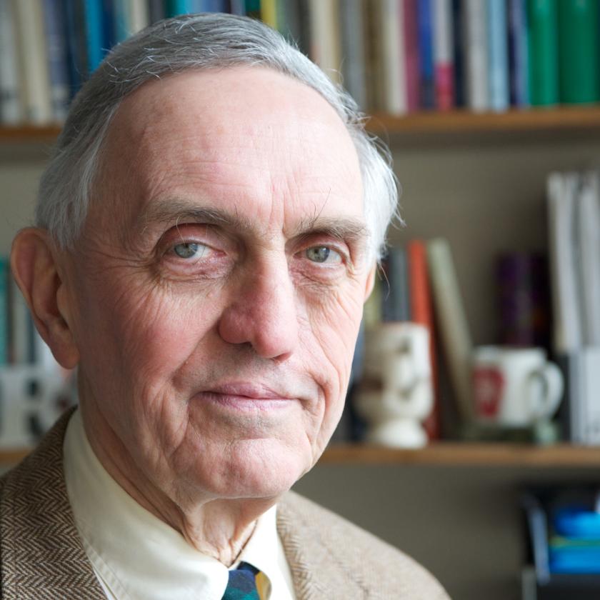 Image of a man in front of a book shelf with a suit and tie smiling at the camera