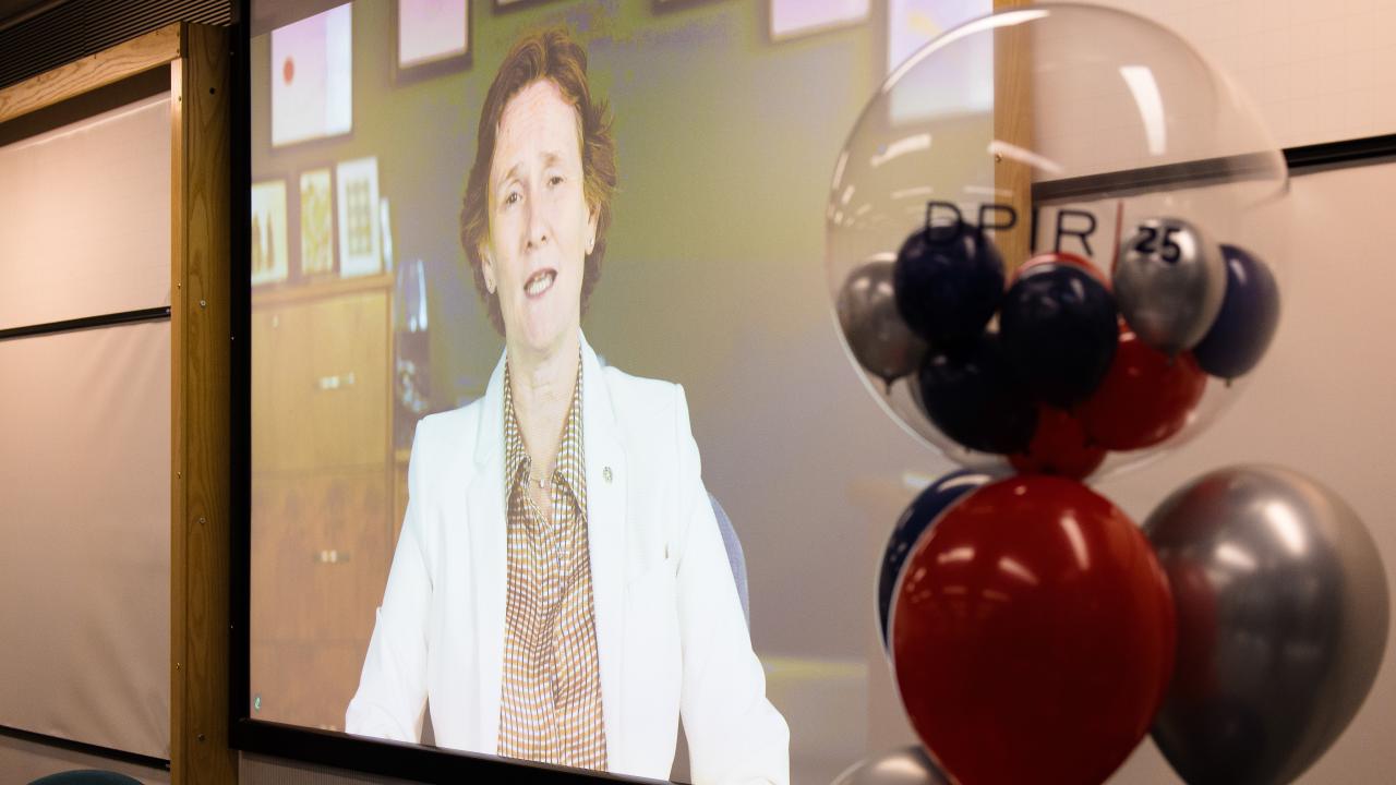 Image of a projector screen with a woman on it with balloons to the right hand side of the screen