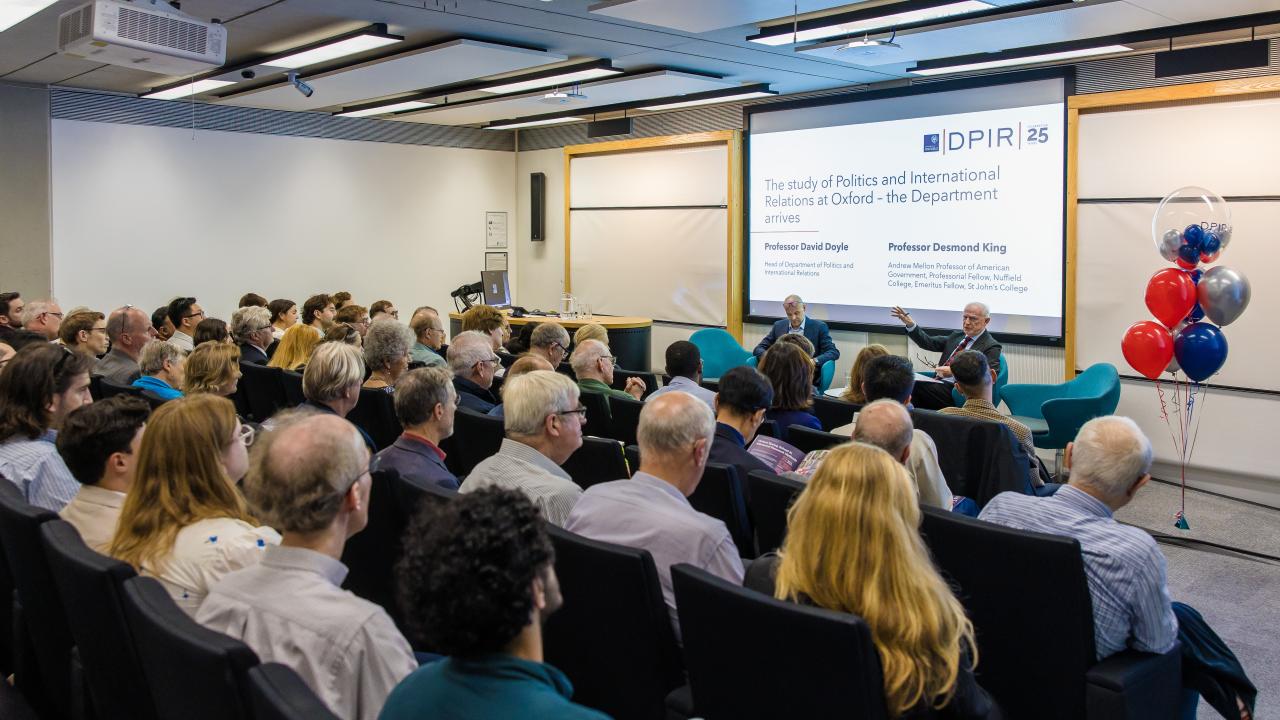 image from behind of an audience listening to a lecture in front of a projector screen