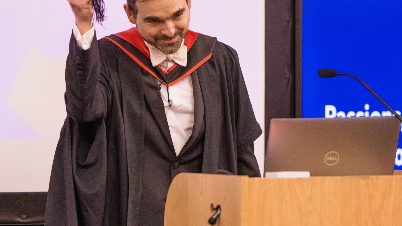 image of a man at a lectern taking off his mortar board