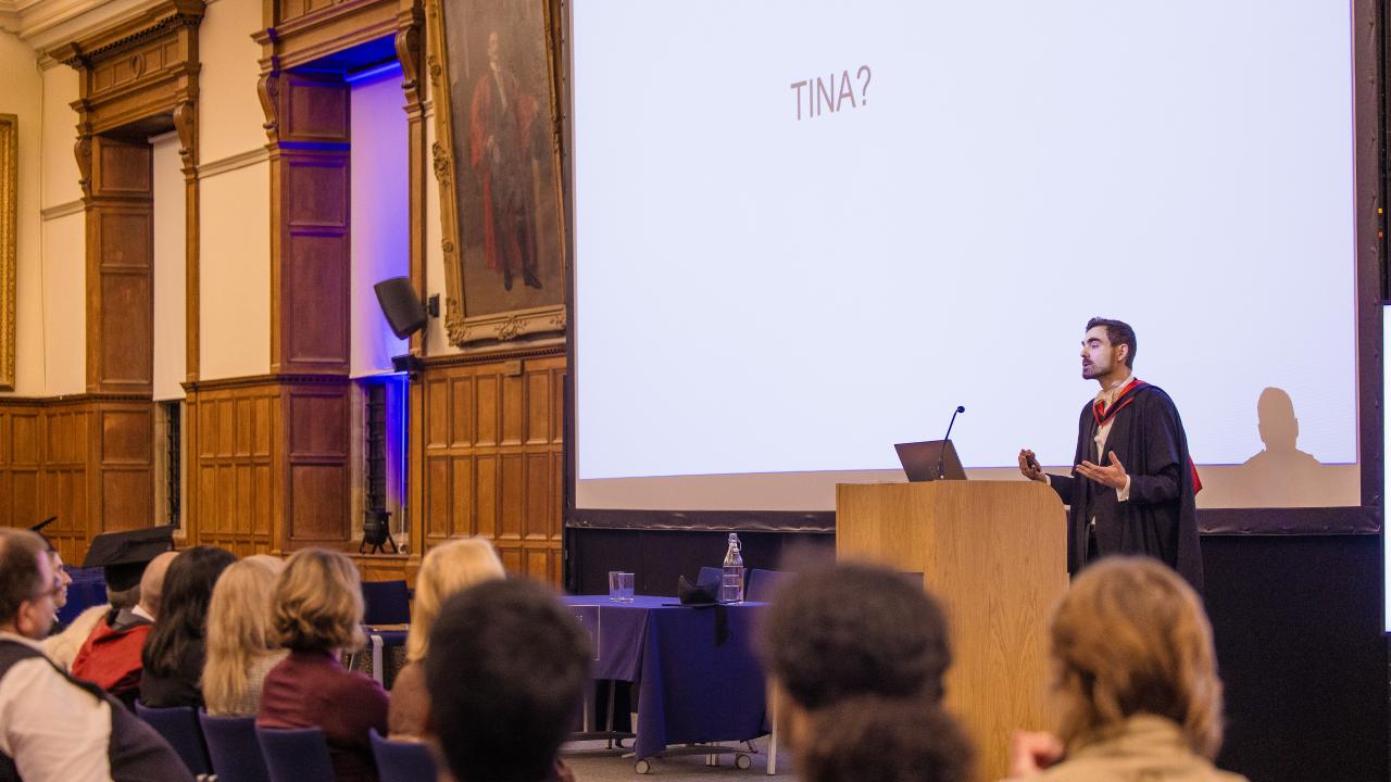 image of a man in front of a lectern in front of a projector screen