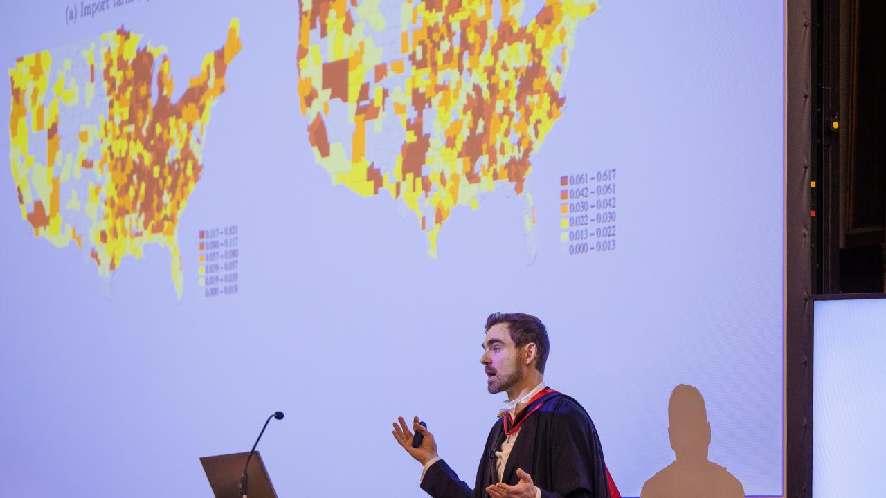image of a man in front of a lectern in front of a projector screen