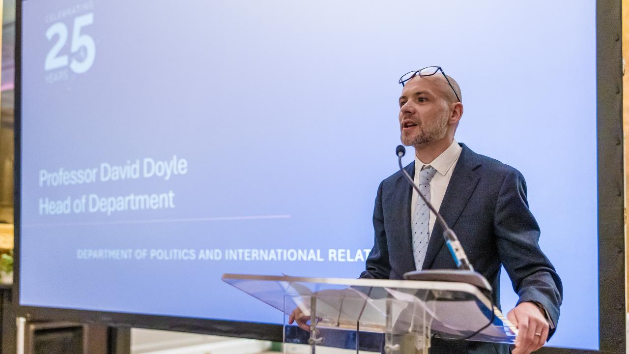 image of a person stood talking at a lectern in front of a projector screen