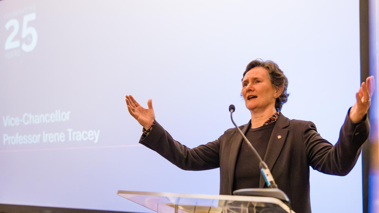 image of a woman with arms raised speaking at a lectern in front of a projector screen