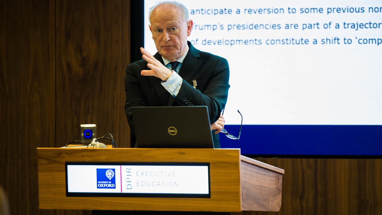 image of a man at a lectern with a projector screen behind him