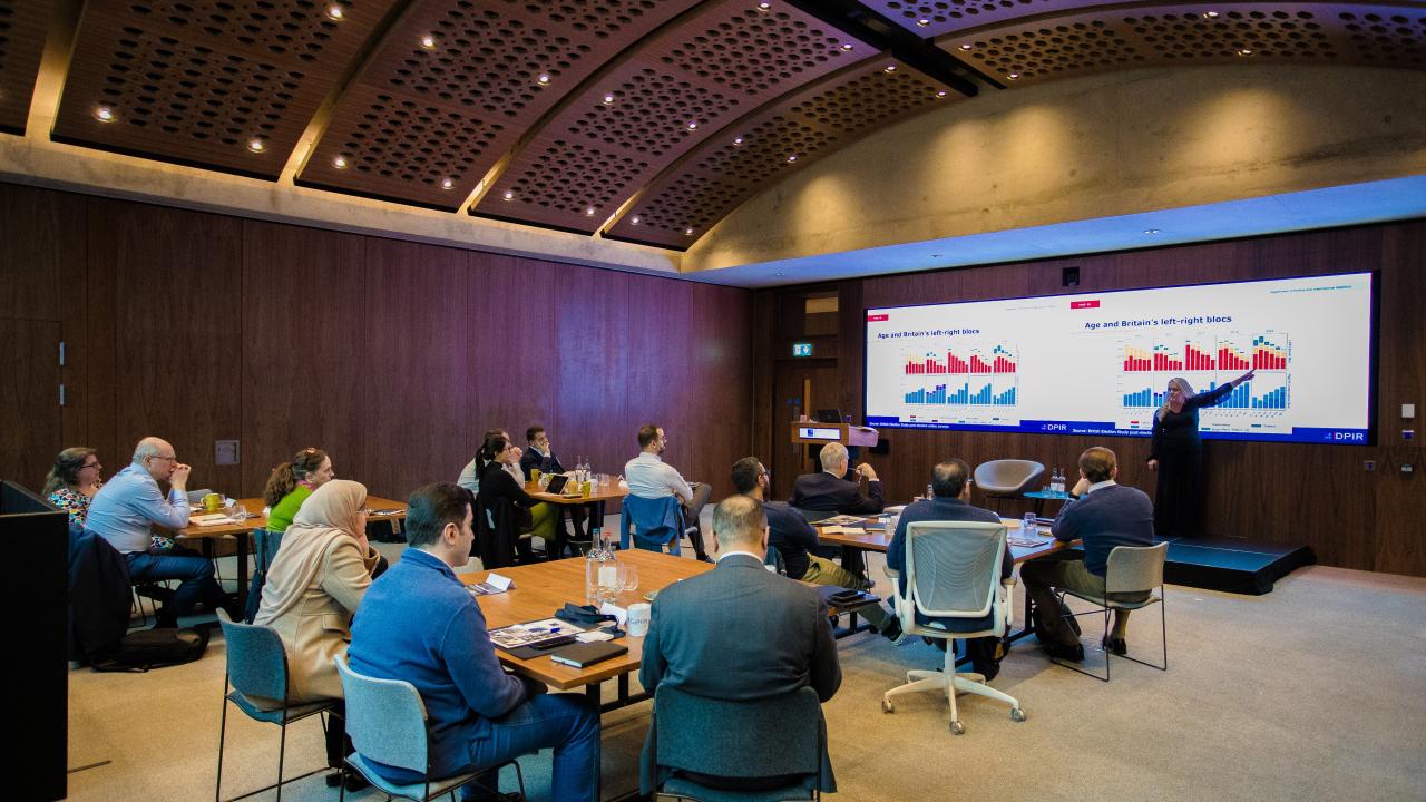 image of an audience sat in a room with a projector screen at the front listening to a lecture