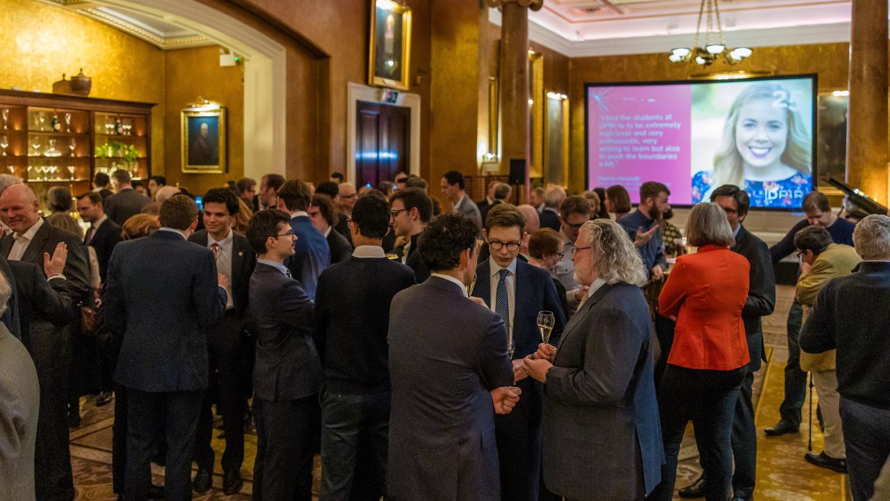 a crowd of people in a room with a projector screen in the background