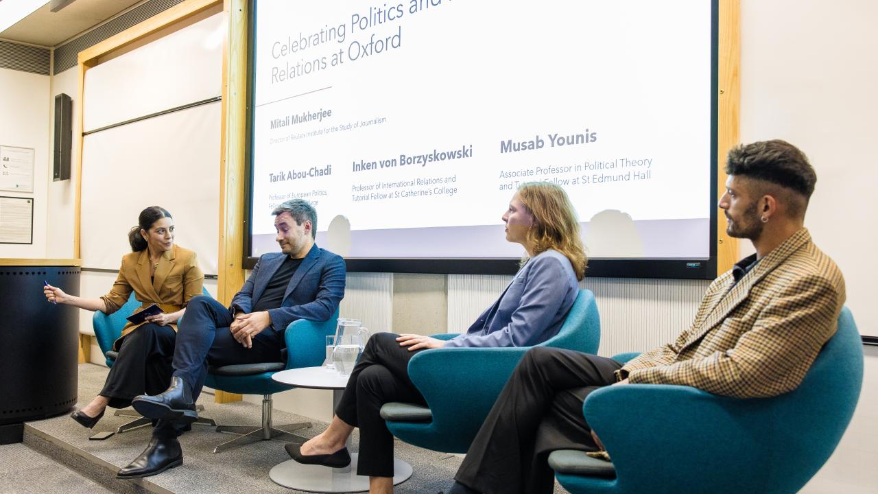 image of a panel of four people on a stage with a projector behind them