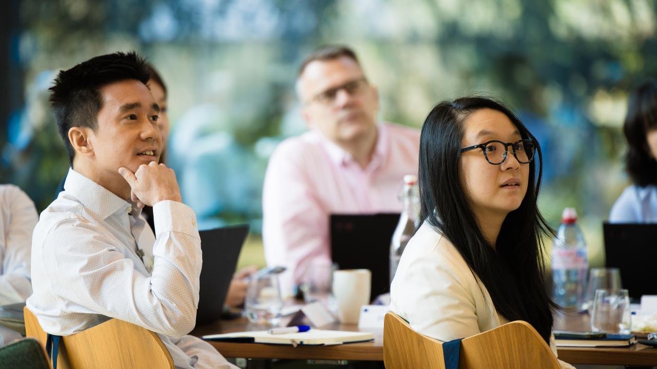 side image of three people sat at tables listening to a lecture