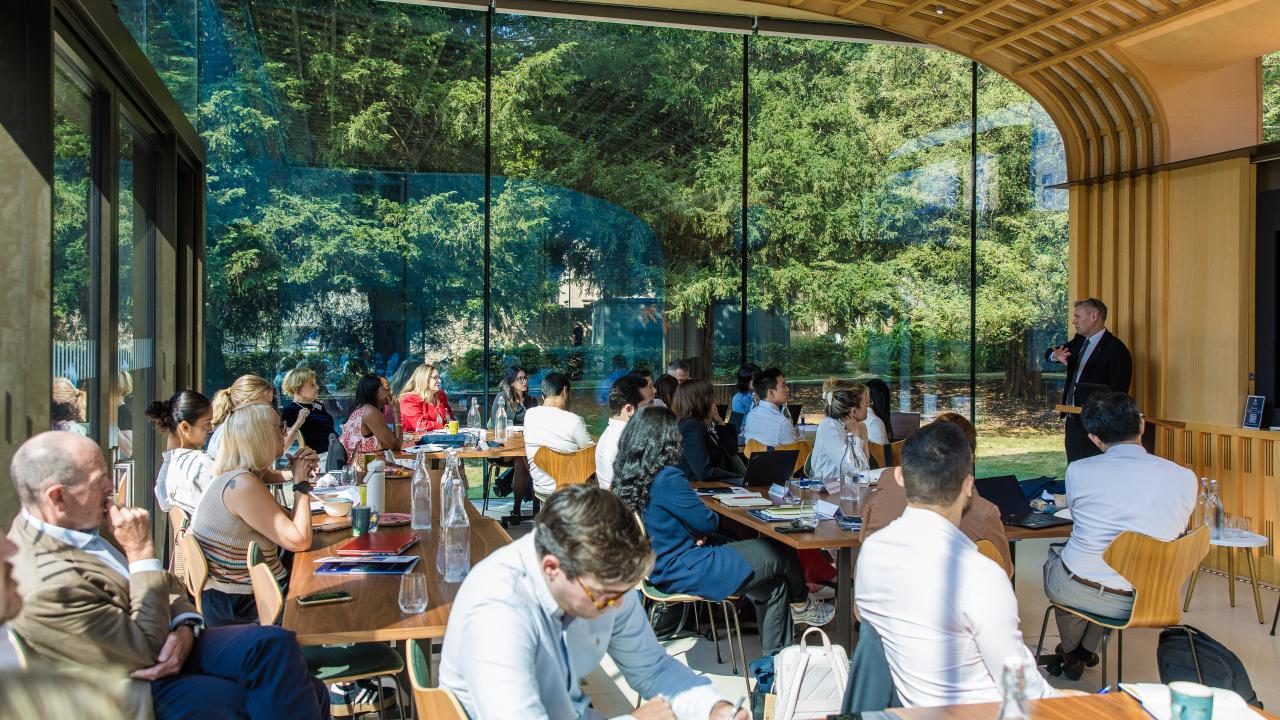 a room full of people seated in a glass-sided room