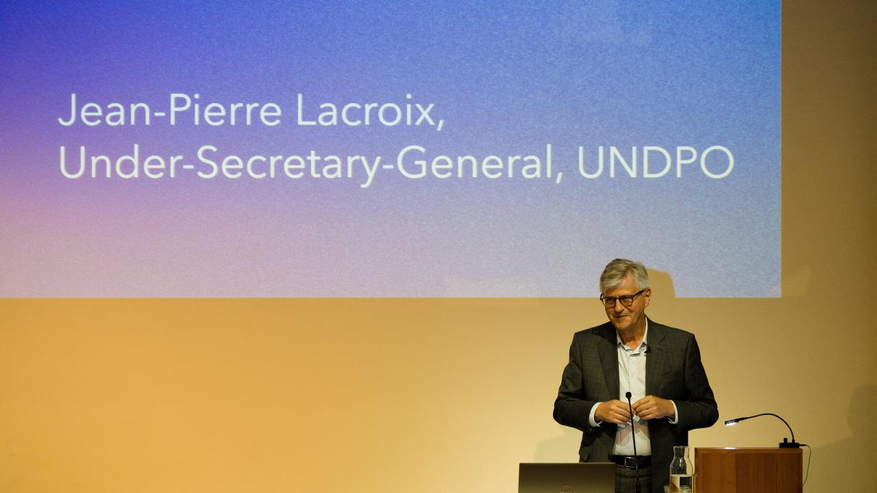 image of a man at a lectern giving a lecture in front of a screen