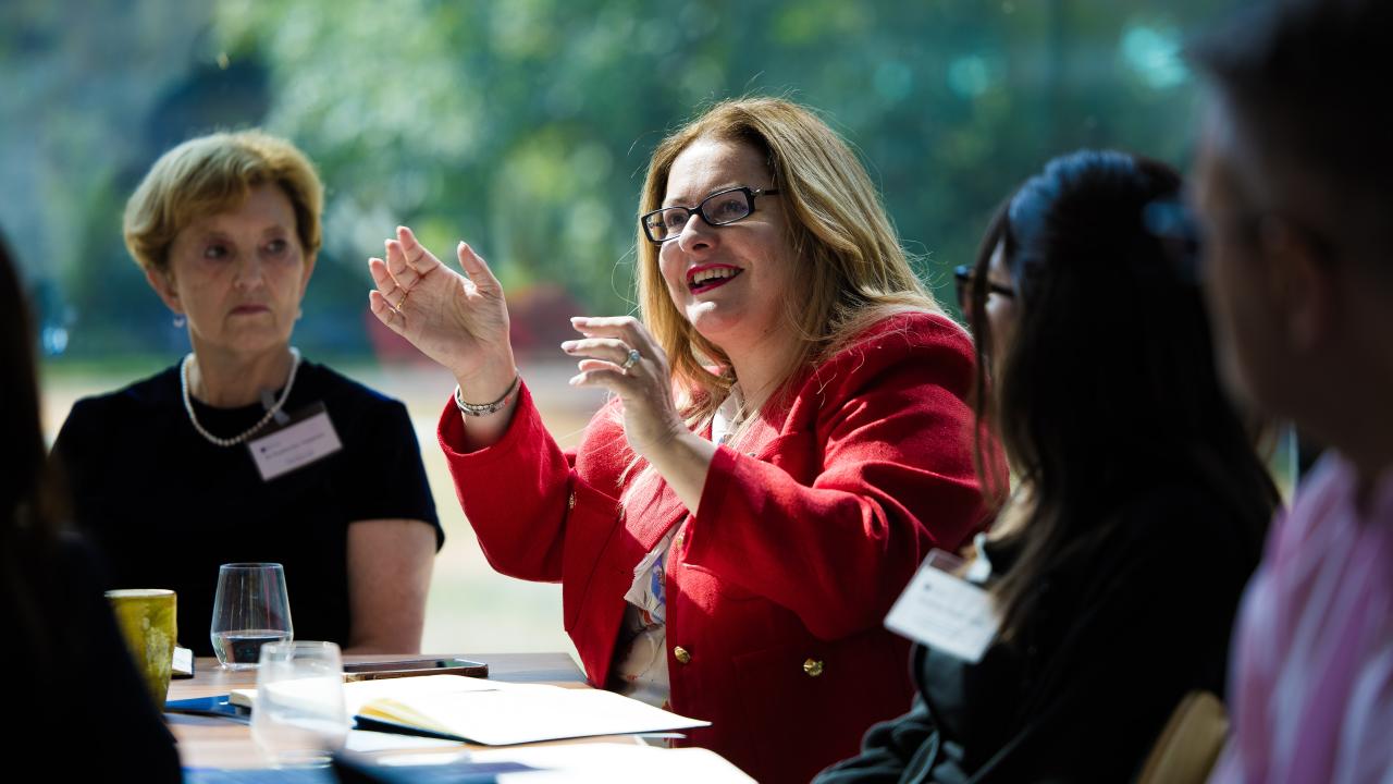 image of a woman in a red top sat gesticulating with people on either side of her