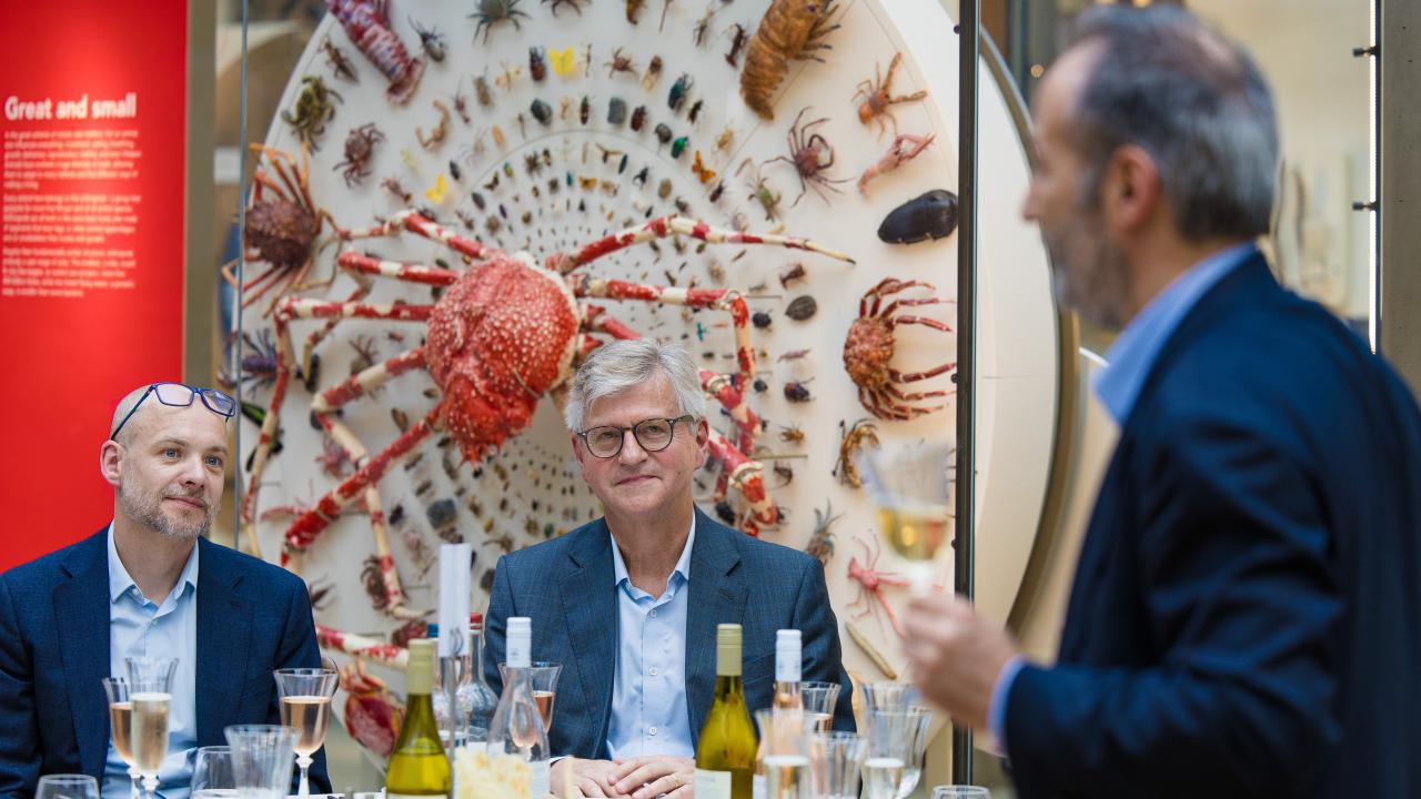 image of a man stood talking to two other men sat at a table