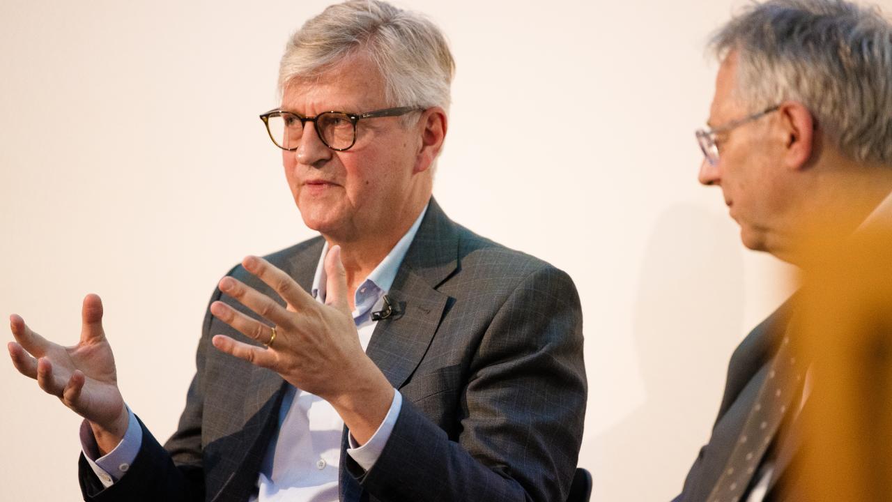 image of two men sat next to one another, the man on the left gesticulating