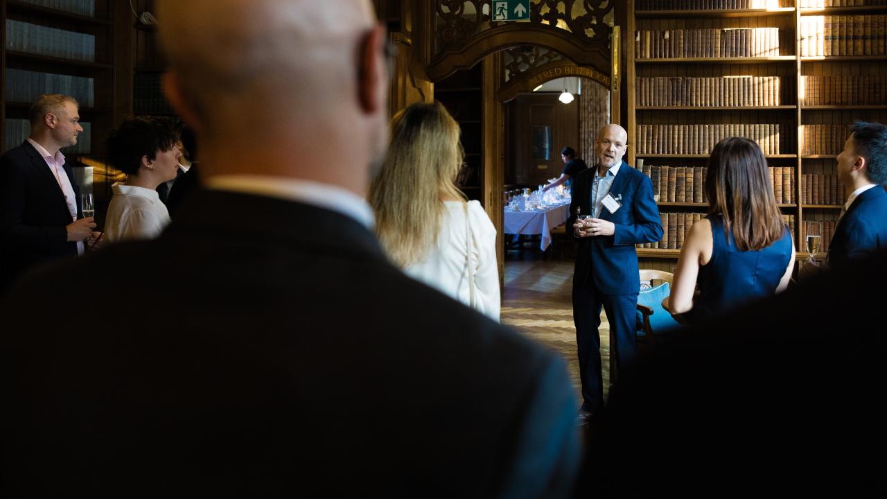 image of a man speaking in the background with the backs of people in the foreground standing