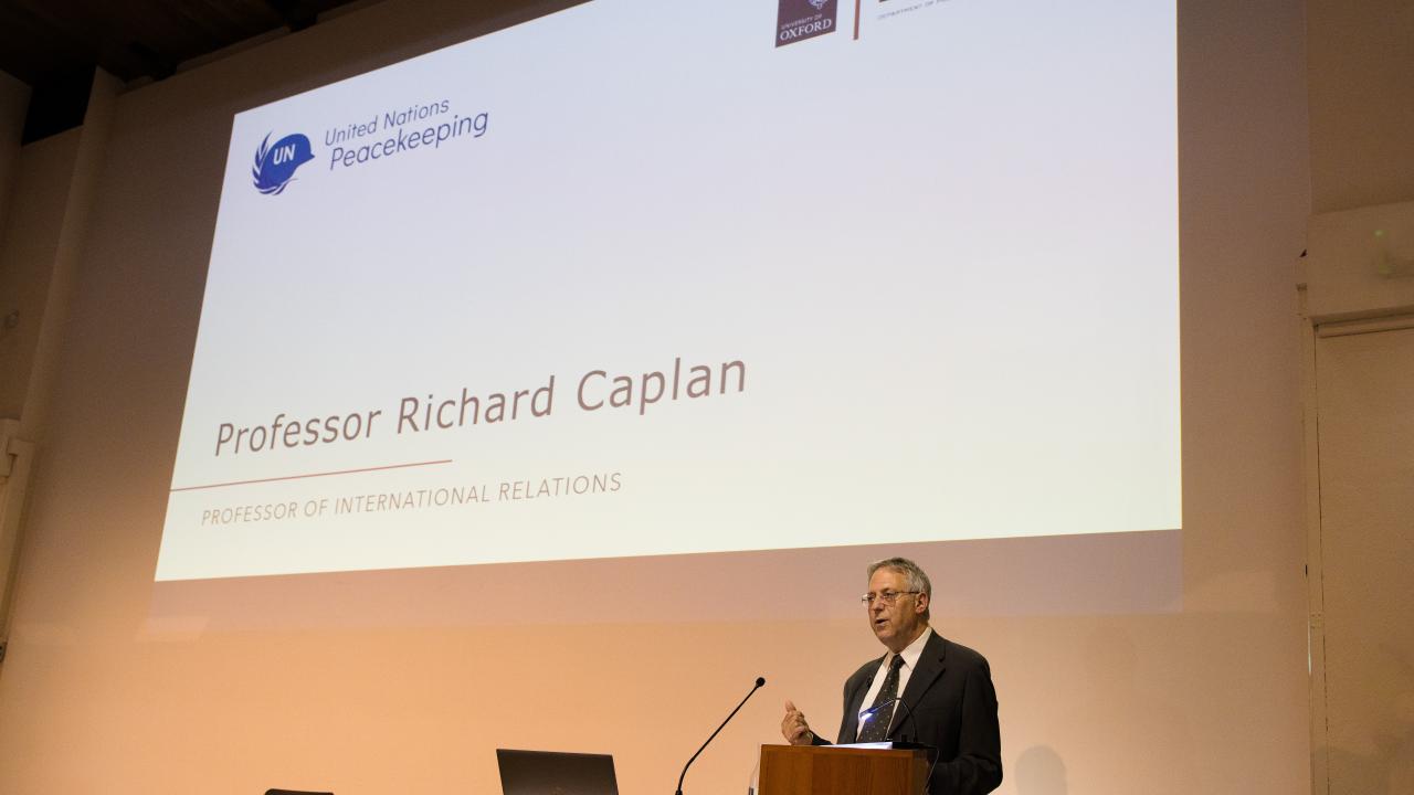image of a man at a lectern giving a lecture in front of a screen