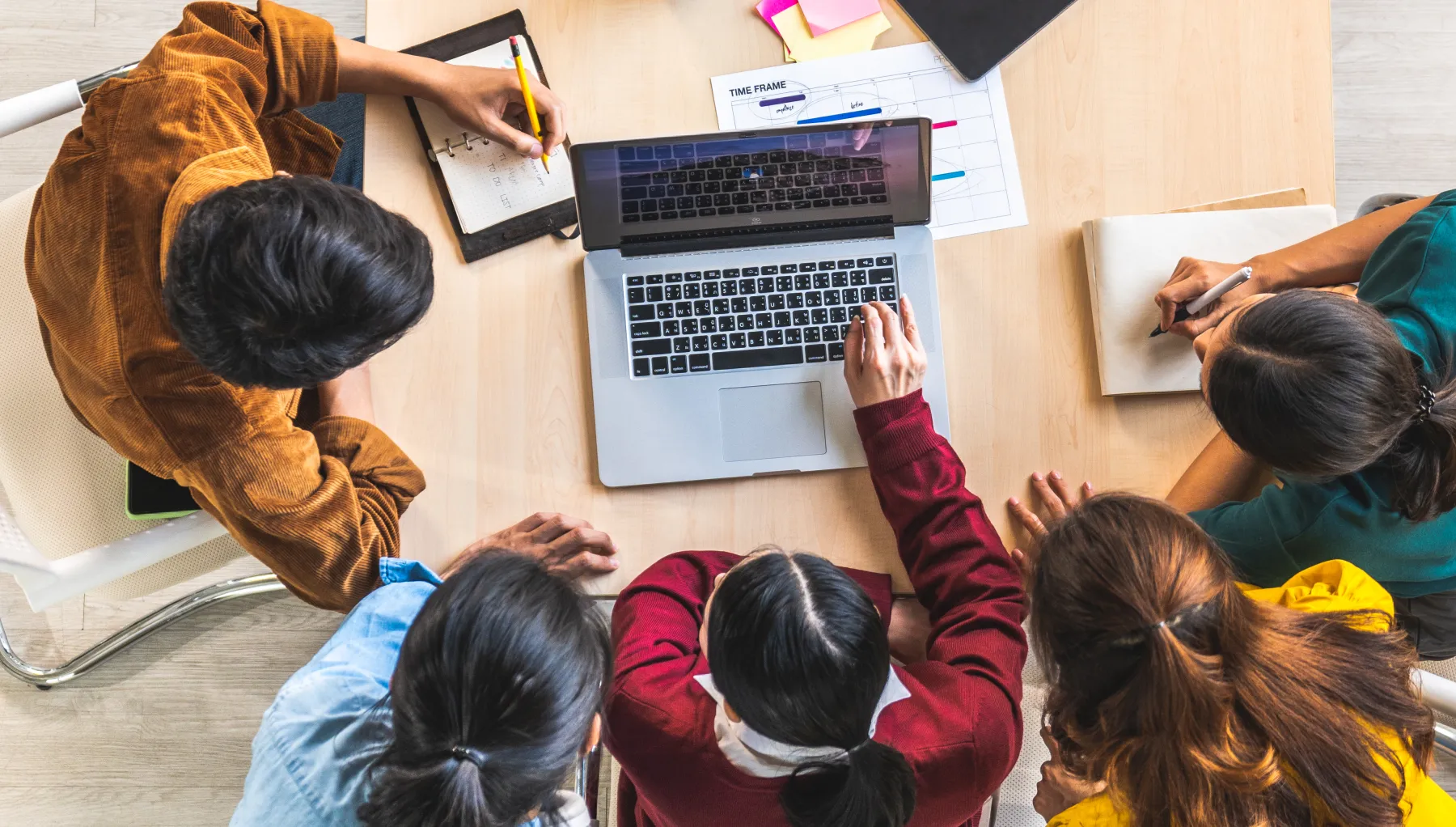 aerial shot of  a group of people huddled around a laptop