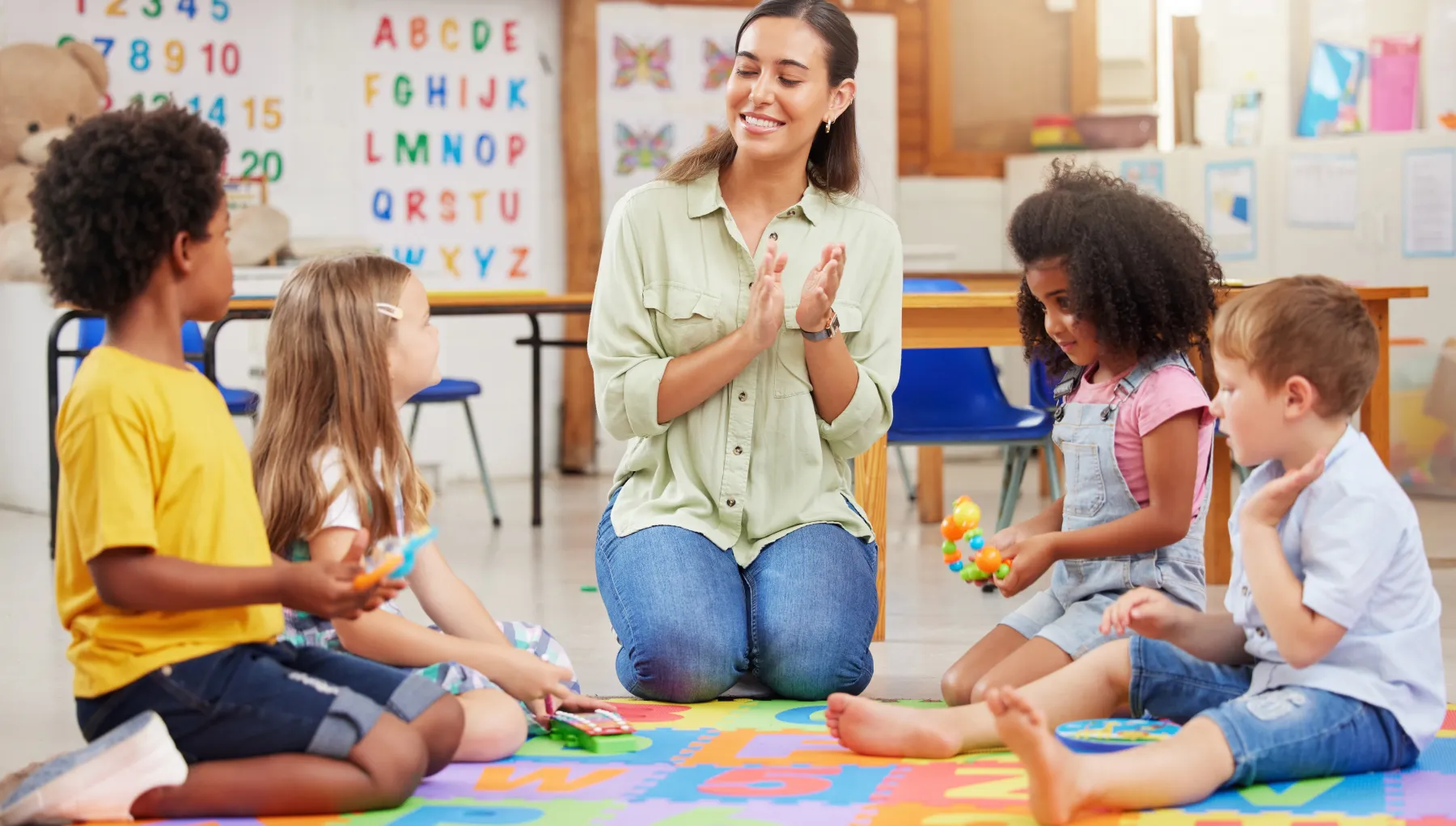 image of a nursery teacher clapping hands with four children beside her