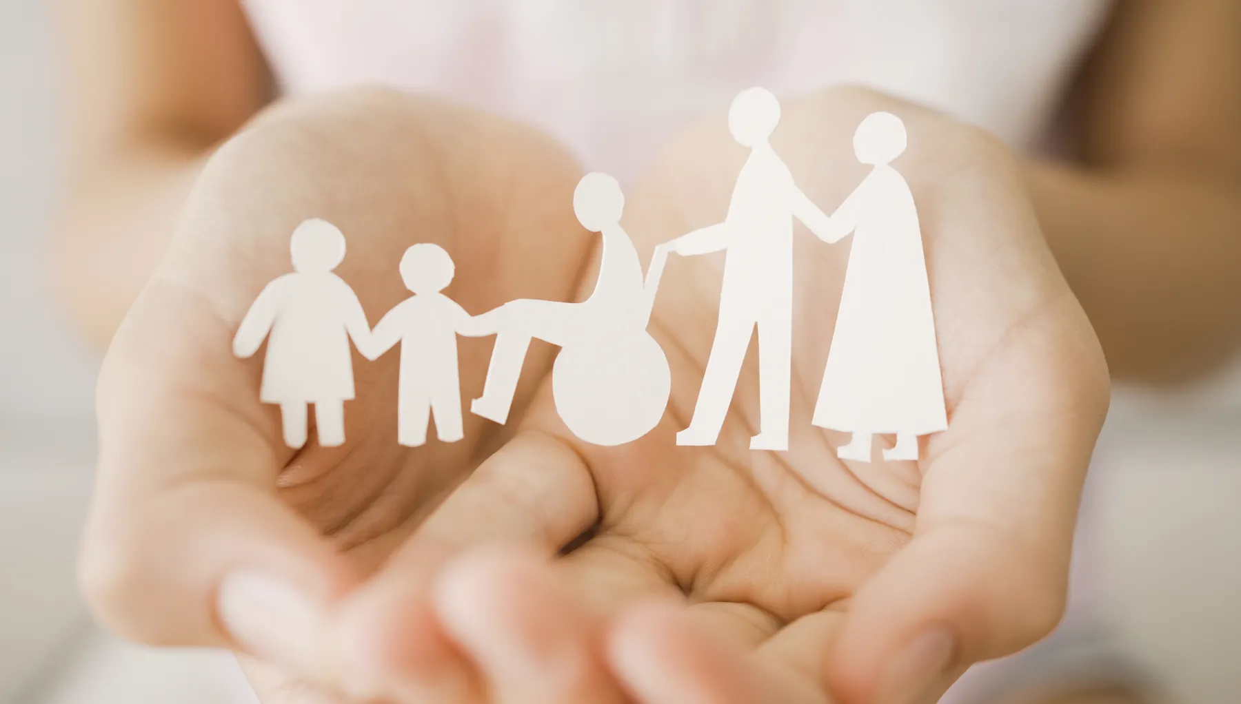 image of a pair of cupped hands with a paper cutout out two children, an elderly couple and a wheelchair user  held in the hands