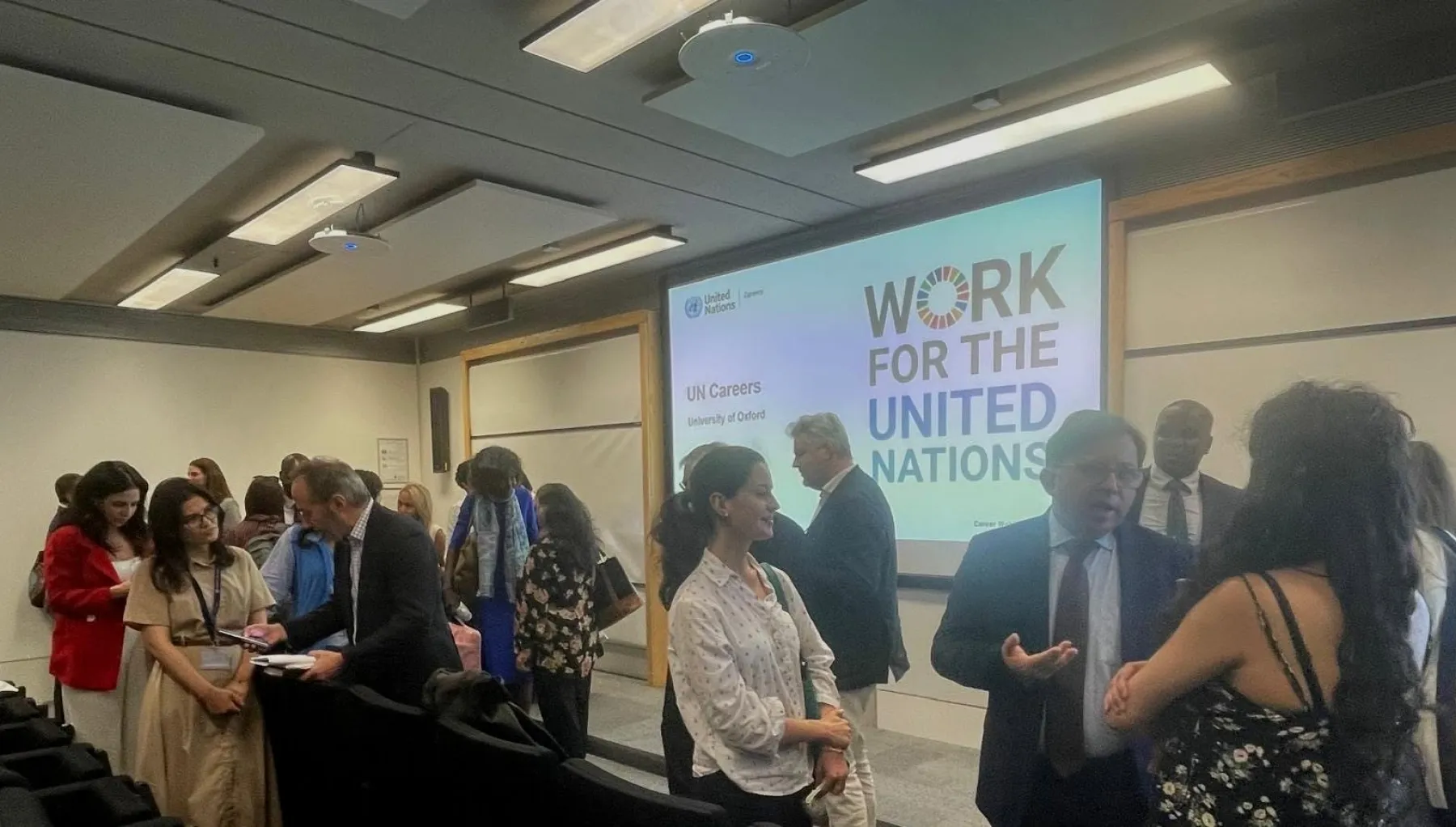 Image of a screen with the words 'Work for the United Nations' on it, with a crowd of people in front of it