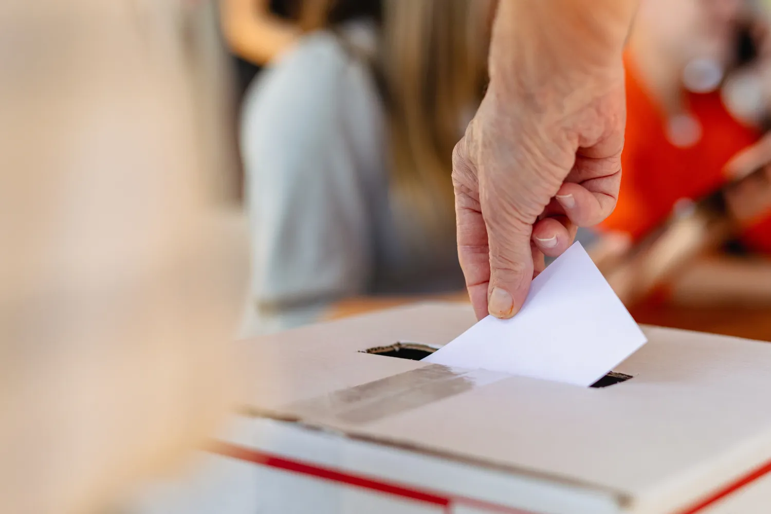 Image of a person'r arm placing a voting slip into a ballot box
