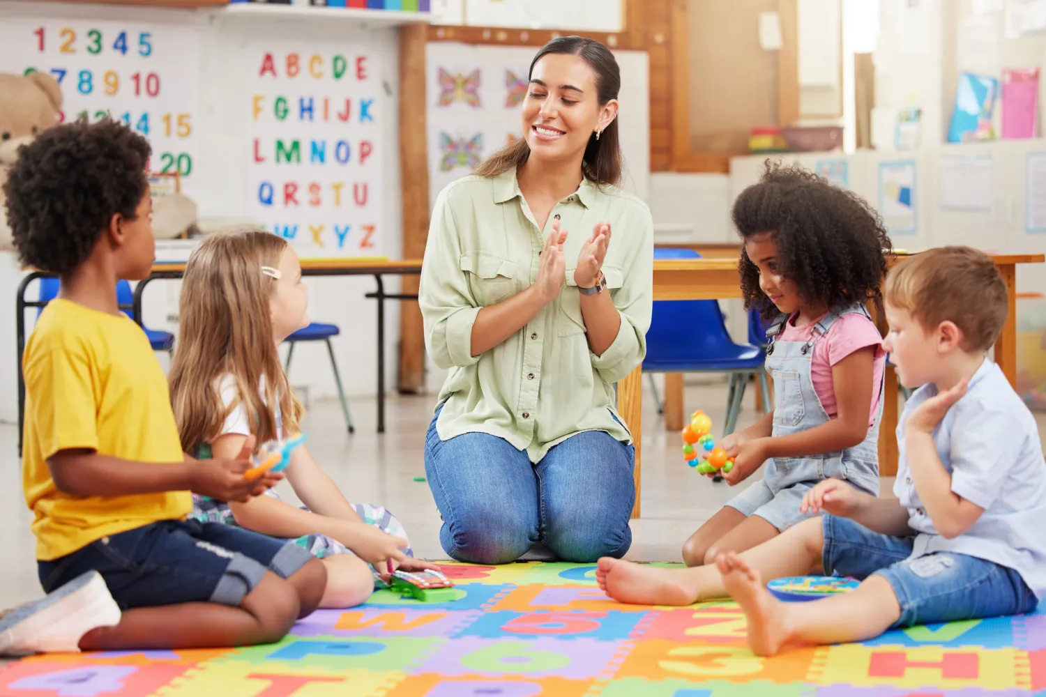 image of a nursery teacher clapping hands with four children beside her