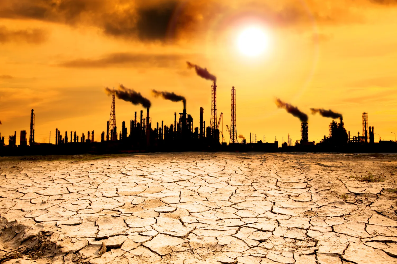 image of a row of chimneys with smoke billowing from them against a backdrop of a sunny orange-coloured sky with a foreground of cracked earth