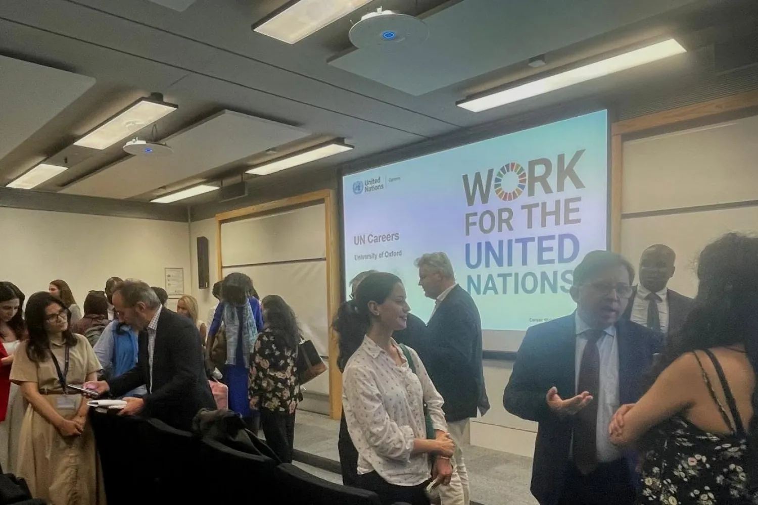 Image of a screen with the words 'Work for the United Nations' on it, with a crowd of people in front of it