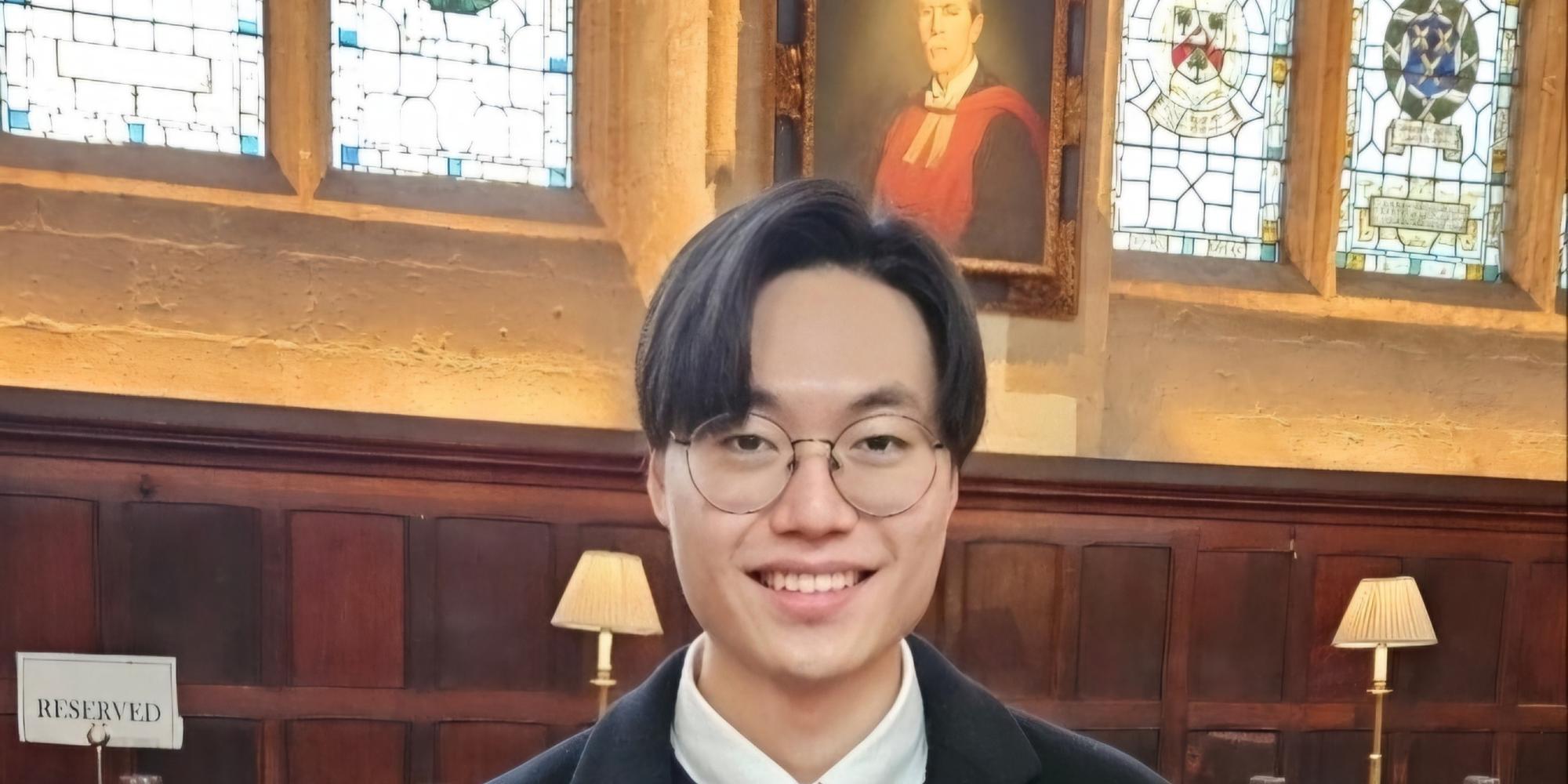 Image of a man wearing glasses and a dark blazer smiling at camera