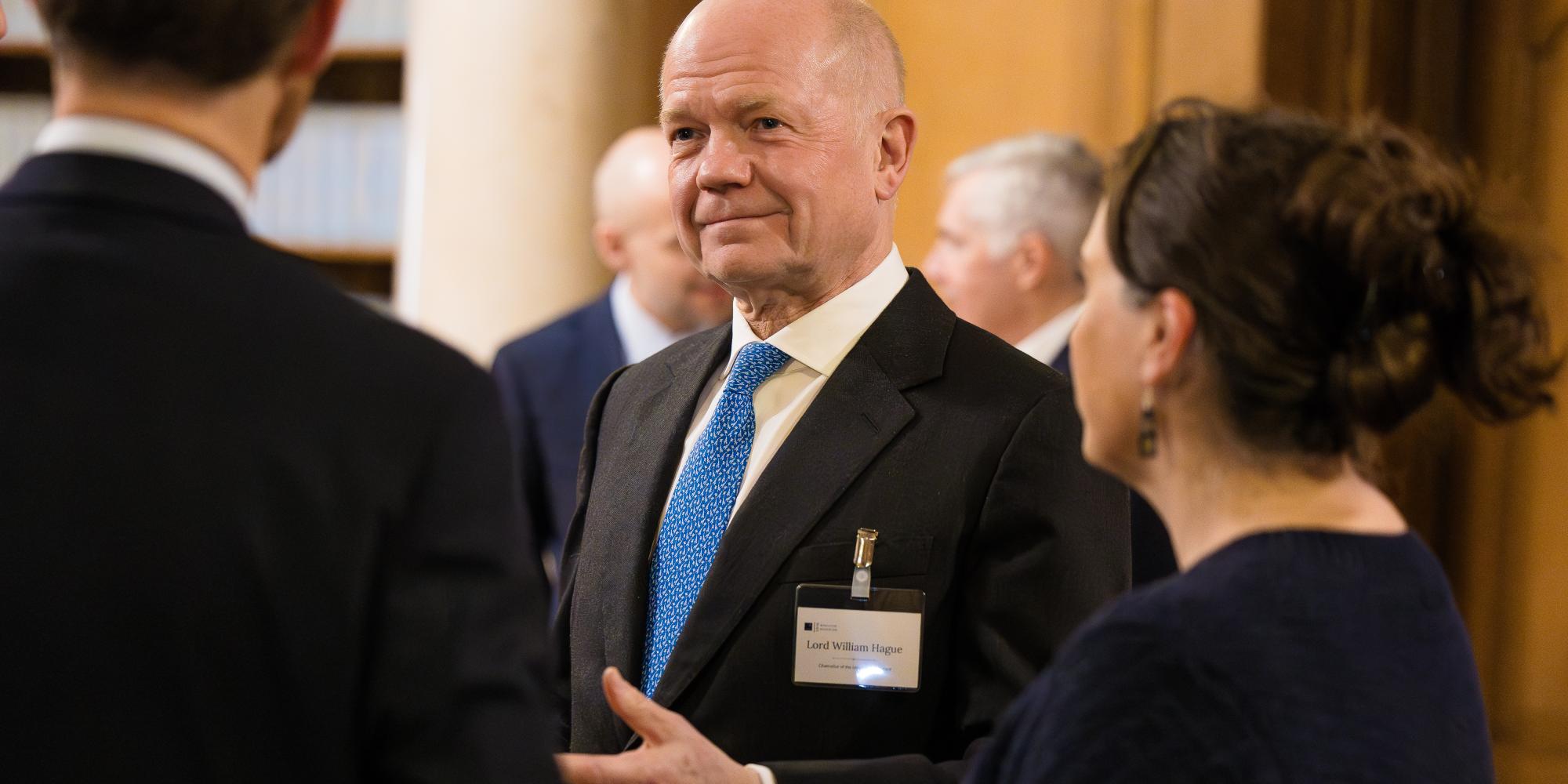 Image of a person in a suit and tie talking to two people with their backs to the camera