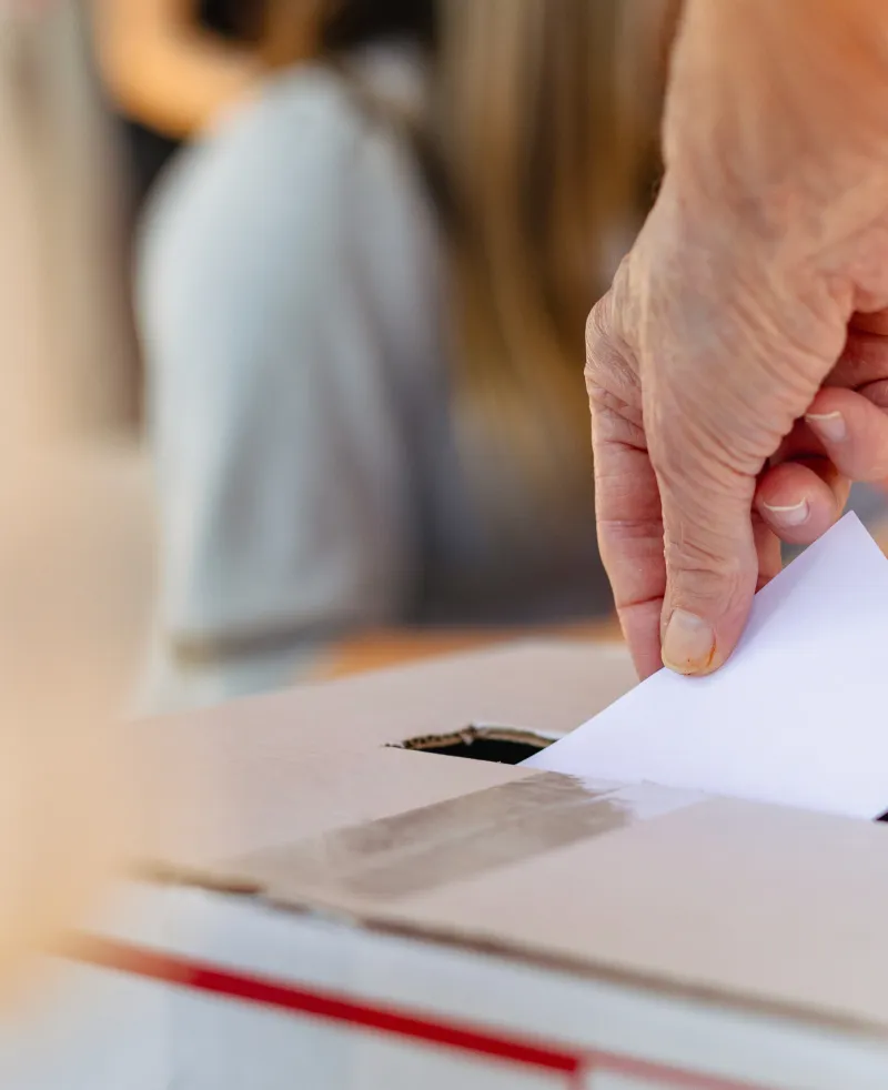 Image of a person'r arm placing a voting slip into a ballot box