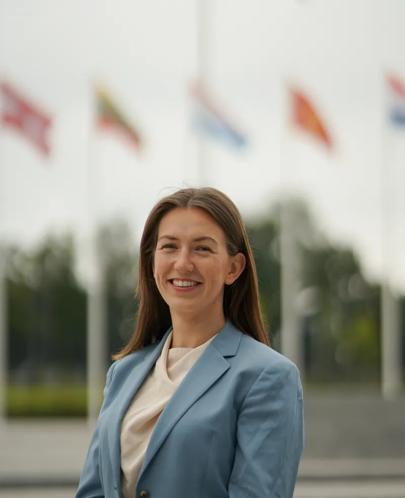 Image of a woman in front of some flags smiling at the camera